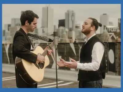 Two musicians standing in front of each other, one with a guitar and the other singing