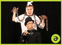 A man with chains around his neck, looking down at a man in a top hat