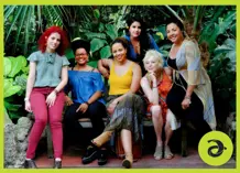 Six women sitting on and around a bench, surrounded by greenery