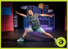 A man on stage, making a funny face and with legs and arms stretched