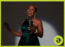Divine Brown in a green dress, with a microphone in front of her